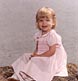 toddler girl in pink dress next to water displays a cheerful smile